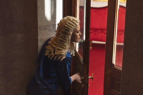 person med Holberg-parykk ser gjennom døråpning