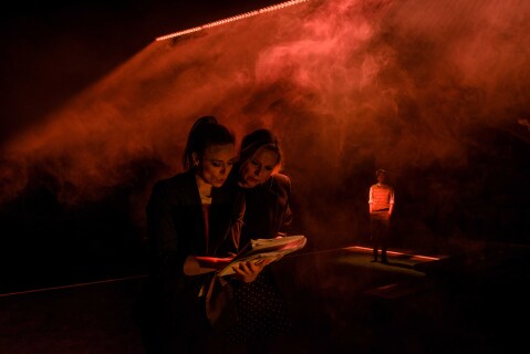 To kvinner leser i et manus på en mørk, røykfylt scene