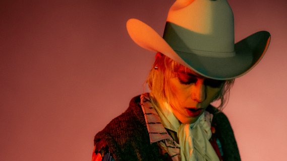 Portrett av kvinne i cowboyhatt som ser ned mot rosa bakgrunn