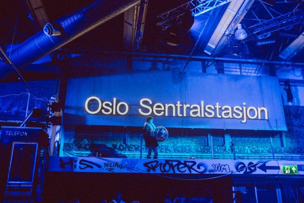 Kvinne står på platå og holder en stor diskokule. På veggen bak står det "Oslo Sentralstasjon"