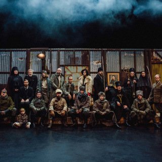 Menn og kvinner i 20-tallsklær foran grønn bølgeblikkvegg