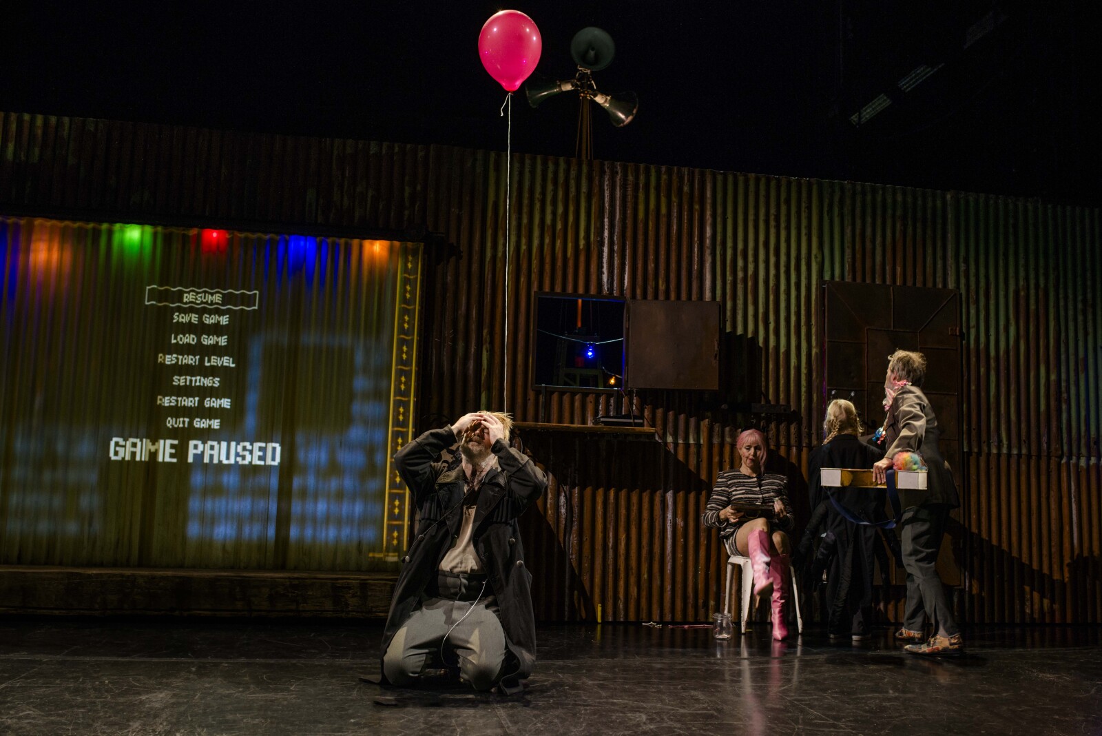 Mann med ballong i en lang tråd sitter på kne og holder seg på hodet. Ved siden av sitter en kvinne og leser, mens to andre personer ser gjennom en luke i veggen. På andre siden står det en spillmeny, med "game paused" i stort