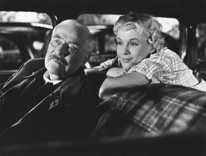 Eldre mann og ung kvinne titter ut av en bil.