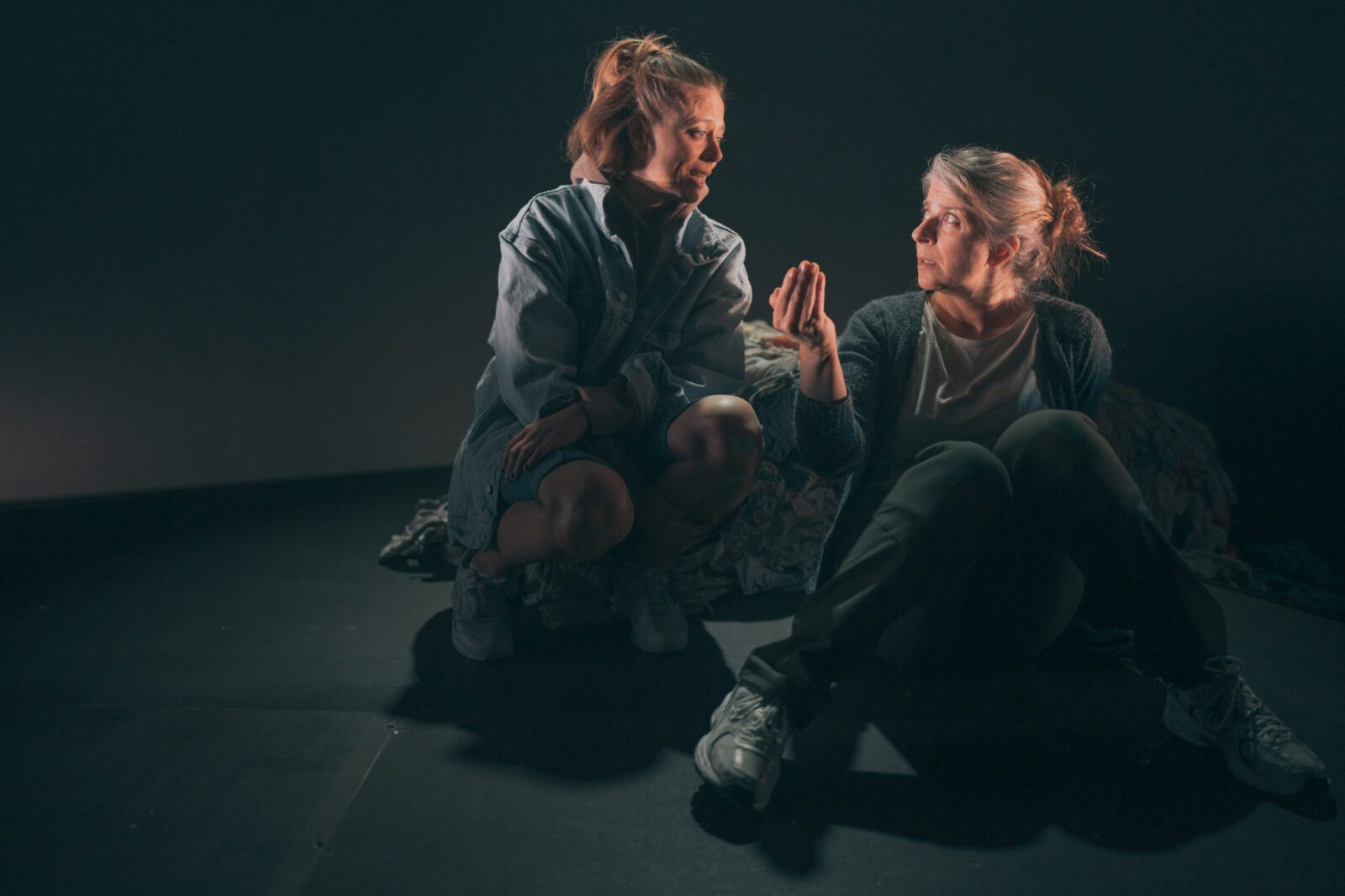 To kvinner sitter og diskuterer på en mørk scene