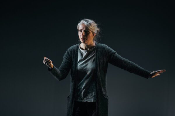 En kvinne står og gestikulerer mot mørk bakgrunn