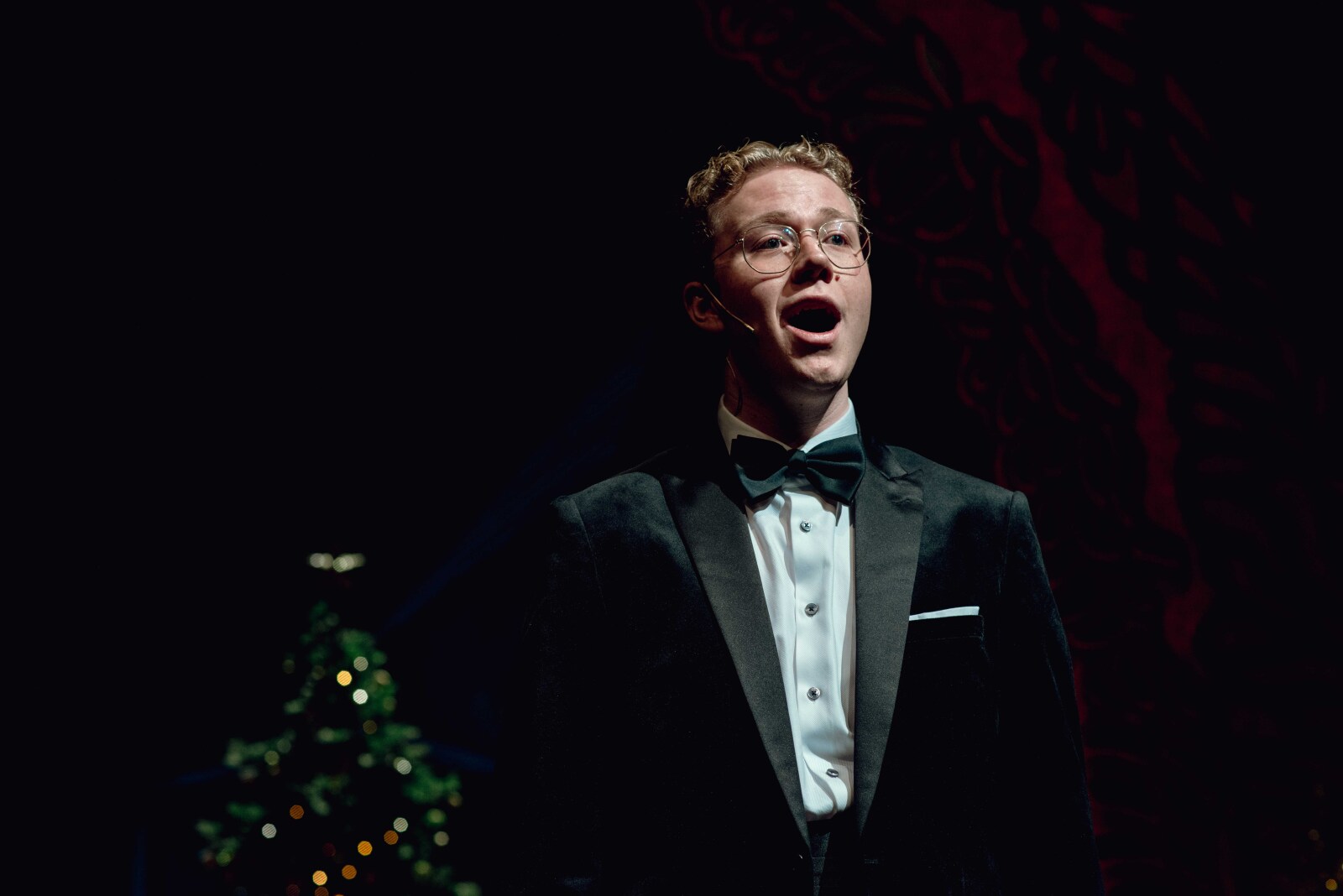 Festkledd skuespiller står og synger på en julepyntet hovedscene