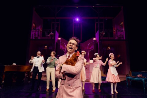 En mann i rosa dress holder en høne i hendene mens han synger.