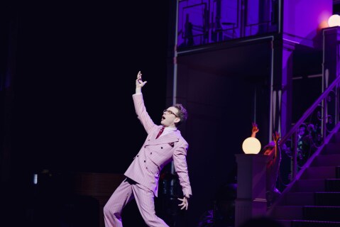 Mann i rosa dress synger på en scene med stor positur