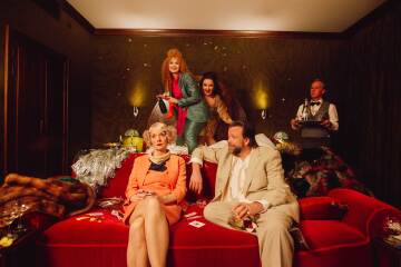 Fire skuespillere som herjer på et hotellrom. To kvinner hopper i senga, mens en kvinne og en mann sitter i sofaen