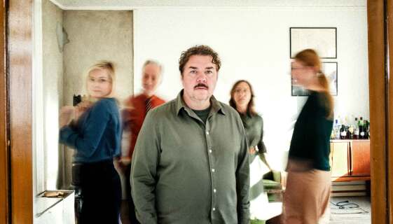 Fem skuespillere i en 60-tallsleilighet. Mannen i midten ser i kamera og er den eneste som ikke er blurry