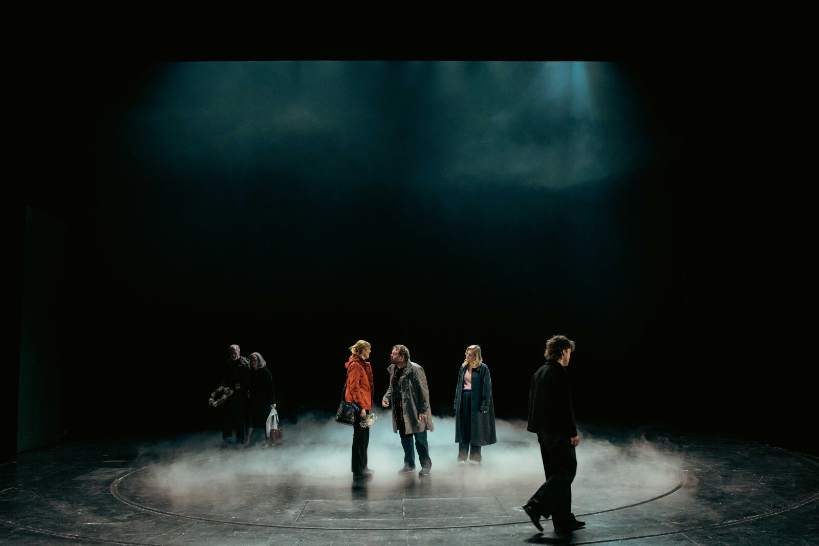 En gruppe på seks personer står spredt i tåke på scenen under dramatisk lys