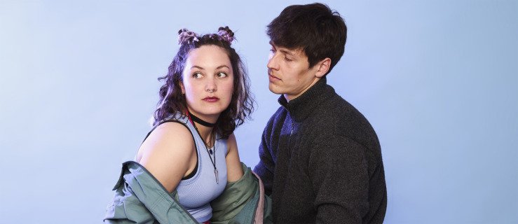 Gutt og jente kledd som ungdommer mot blå bakgrunn. Gutten ser på jenta, mens hun ser bort