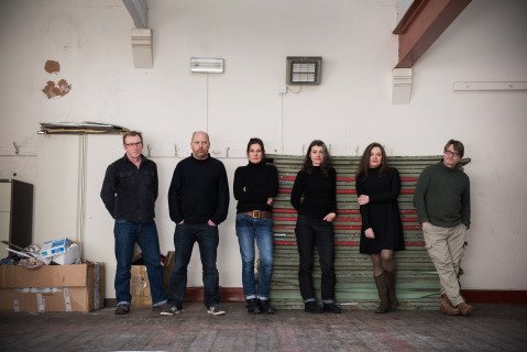 Three men and three women on a line in front of a white wall