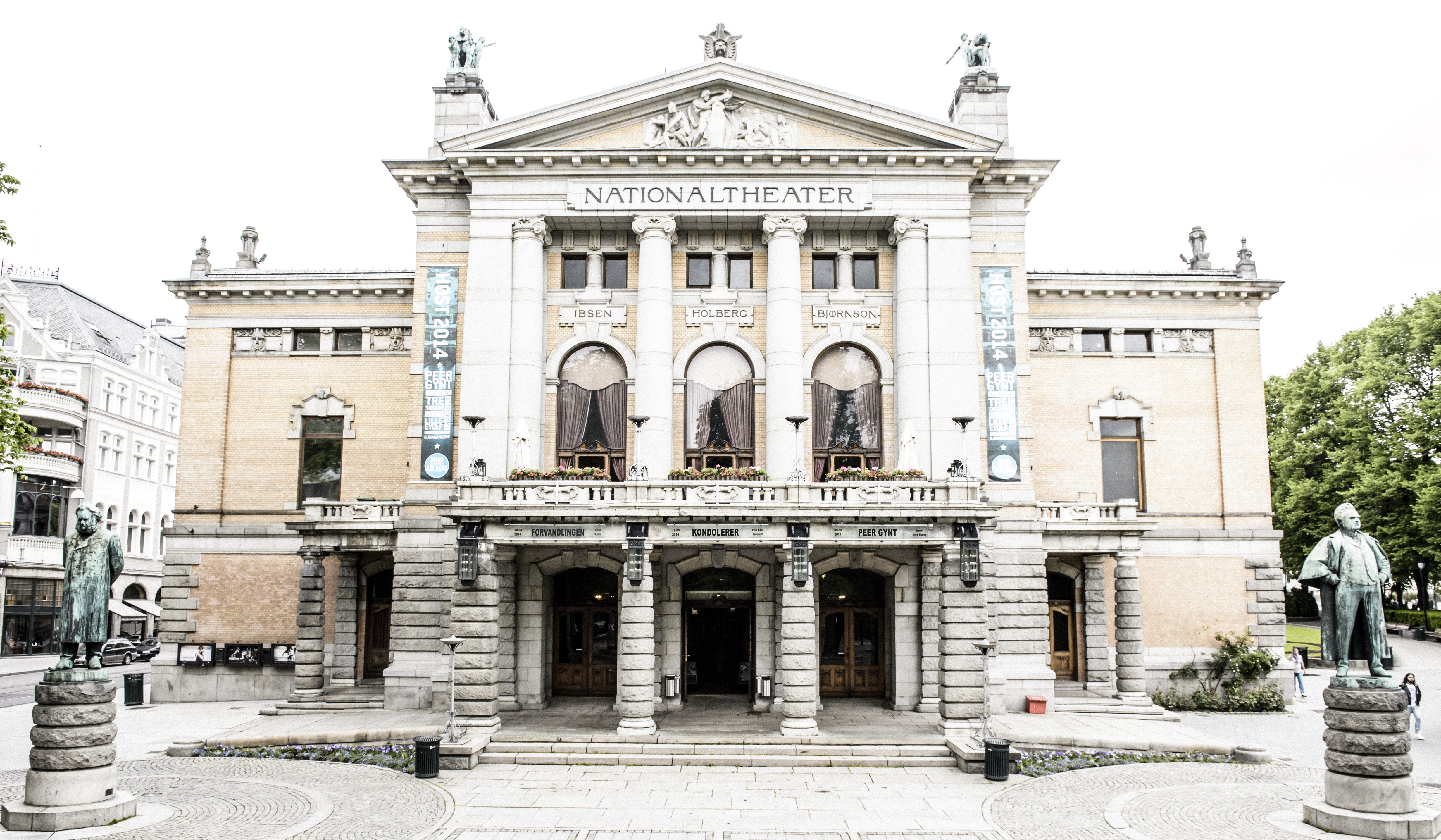 Nationaltheatrets fasade avbildet i overskyet dagslys med statuene av Ibsen og Bjørnson i hver sin kant.