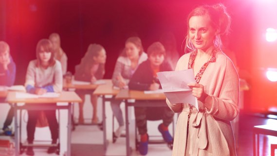 Kvinne i 30-årene står foran en klasse og holde noen papirer.